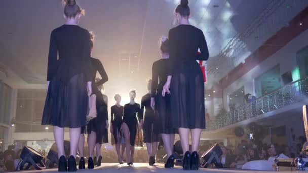 Неделя моды, групповые модели на высоких каблуках в одинаковых черных прозрачных платьях со стильными сумочками выходят на подиум на презентации новой дизайнерской коллекции в центре внимания — стоковое видео