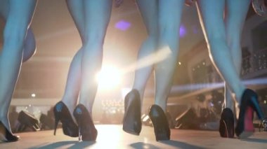 Yüksek topuklu ayakkabılı mankenlerin ince bacakları moda etkinliğindeki spot ışıklarının altında podyumda sıralanır.