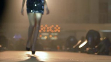 Yüksek topuklu uzun bacaklı ince model kız moda etkinliğinde podyumda dikkatsiz arka planda yürüyor.