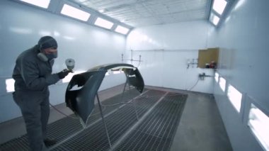 Otomobil boyama, koruyucu takım elbiseli teknisyen erkek araba merkezindeki parlak ışıklandırılmış özel atölyede aracın bir kısmını boyuyor.