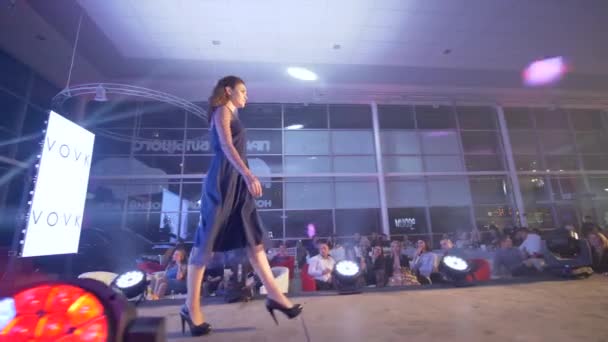 Стильная модель на высоких каблуках в вечернее черное платье оскверняет подиум на показе мод в прожекторе — стоковое видео