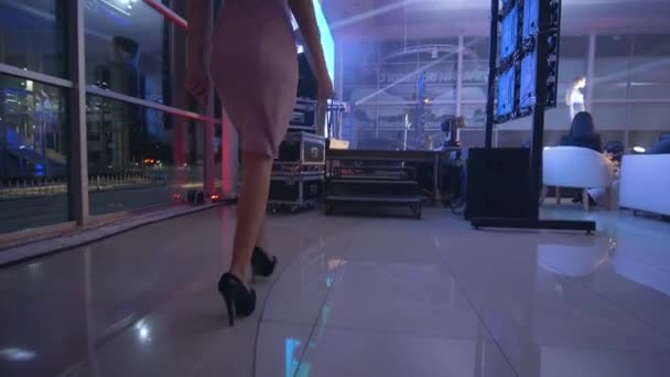 Jovem modelo pódio em sapatos de salto alto em vestido elegante apresenta coleção designer na semana da moda em holofotes — Vídeo de Stock