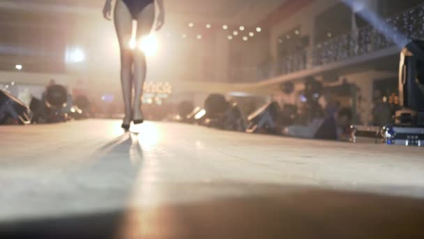 Desafiar show, mulher modelo em roupa de banho designer Em saltos altos caminha na passarela em holofotes fora de foco na apresentação da coleção — Vídeo de Stock