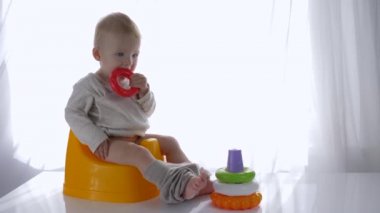 Şirin küçük çocuk lazımlığa oturmuş ve parlak odada eğitici plastik oyuncak piramidiyle oynuyor.