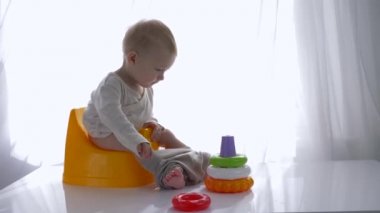 Gelişmekte olan bebek lazımlıkta oturuyor ve parlak odada eğitici renkli oyuncak piramidiyle oynuyor.