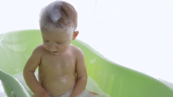 Bathing baby, little child into foam sitting in water in bath at bright room — Stock Video