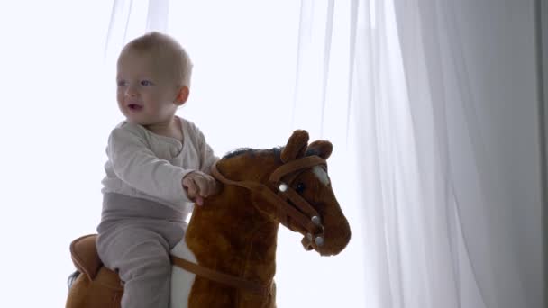 Bonito infantil menino desfrutar balançando no brinquedo cavalo em casa — Vídeo de Stock