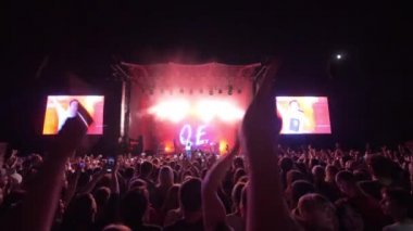 Gece hayatı, kalabalık rock konserinde el çırpıyor. Büyük ekranlı, parlak bir sahneye karşı.