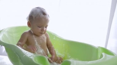 Aydınlık odada banyoda hijyen prosedürleri sırasında köpüklü suya atılan aktif bebek.
