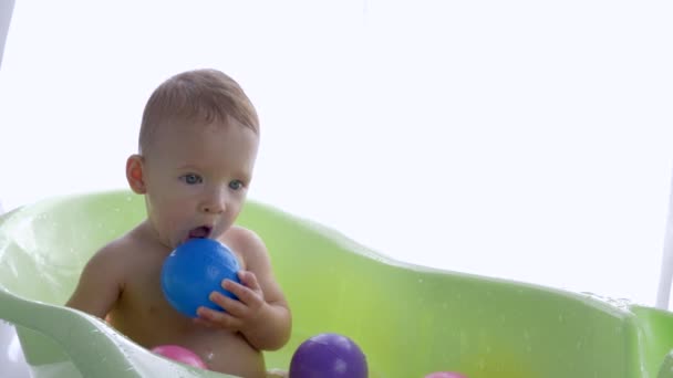 Gelukkig zuiver kid jongen wil uit van in bad met gekleurde ballen na het baden in heldere kamer — Stockvideo
