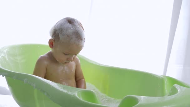 Child care, cheerful kid into suds splashing water in bath in bright room — Stock Video