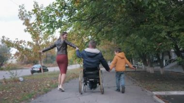 Aile desteği, tekerlekli sandalyedeki neşeli engelli adam mutlu bir şekilde ailesiyle el ele tutuşuyor neşeli bir eş ve güzel bir sonbahar caddesinde yürüyen neşeli bir oğul.