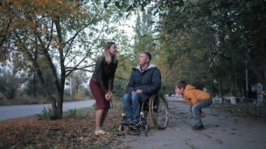 Tekerlekli sandalyede sakat bir aile babası, çocuklu mutlu bir eş, sakat bir babayla parkta oynuyor.