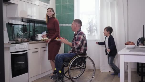 Висить з сім'єю, чоловік у інвалідному візку насолоджується щасливим проведенням часу з дружиною та дитиною на кухні під час приготування їжі — стокове відео