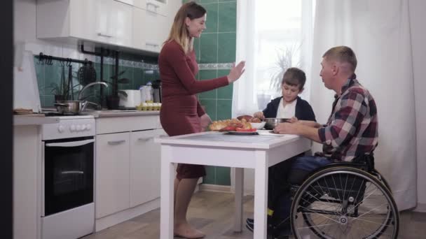 Padres felices, padre discapacitado se divierte con la esposa cariñosa y un hijo feliz mientras cocina para su familia — Vídeos de Stock