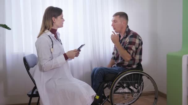 Menselijke gezondheid, medisch onderzoek van een man in een rolstoel door een vrouwelijke arts in omstandigheden die comfortabel zijn voor de patiënt — Stockvideo