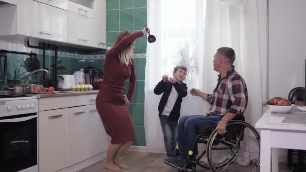 Tekerlekli sandalyedeki adam ve sevgi dolu ailesi mutfakta eğleniyor, dans ediyor ve dostça bir atmosferde yemek pişiriyor. — Stok video
