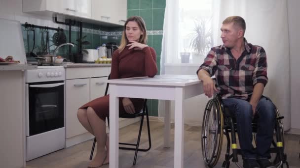 Pelea en la familia, marido molesto, persona discapacitada en una silla de ruedas, maldiciones con su obstinada esposa triste en la cocina, escándalo familiar — Vídeos de Stock