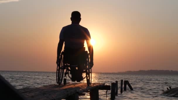 Ill male in wheel chair resting and raises his arms backdrop of skyline near water on summer travel — Stock Video