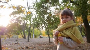 Çocuk sonbahar parkında oynuyor, kadın çocuk arka planda sabun köpüğü üflüyor.