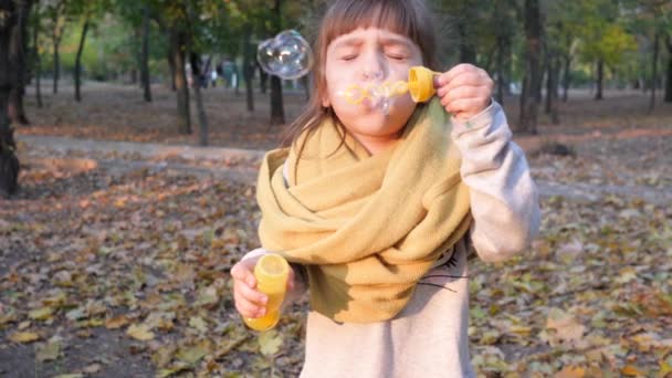 Красивый ребенок делает радужные мыльные пузыри в камеру на открытом воздухе осенью — стоковое видео