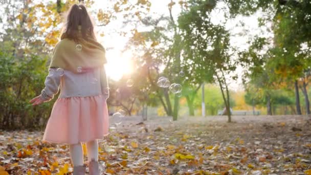 Małe słodkie dziewczyna gra z bańki mydlane w podświetleniu jesienią park — Wideo stockowe