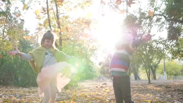 Осінній міський парк, діти стрибають і кидають листя на тлі дерев і листя на сонячному світлі — стокове відео