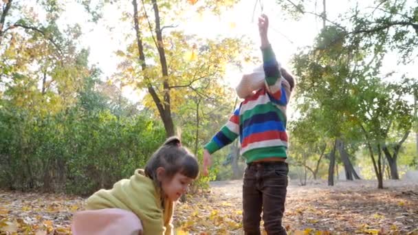 Přátelé házejí velké množství listí do vzduchu ve zpomaleném filmu a užívají si podzimní den v podsvícení — Stock video