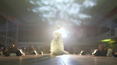 Mankenlerin üzerinde tüyleri olan tasarımcı kıyafetleri seyircilerin önünde podyum boyunca yürüyor.