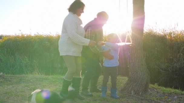 Joyfull weekend of old people and little boy with dog on nature to small lake in sun rays — Stock Video