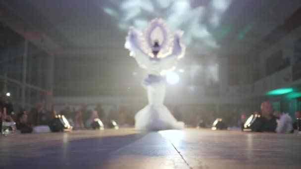 Exclusive white dress with feathers and designer headdress on model posing on runway against backdrop of spotlights and smoke — Stock Video