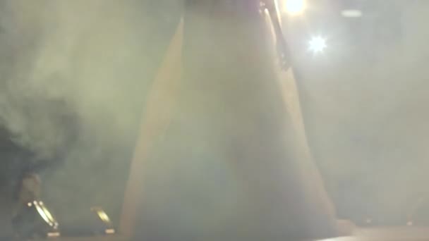 Modelo en vestido elegante blanco entra en el humo a lo largo de la pasarela en cámara lenta en el desfile de moda — Vídeo de stock