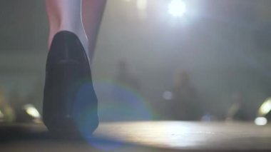 İnce mankenin bacaklarındaki şık ayakkabılar spot ışıklarıyla podyumda yürüyor.