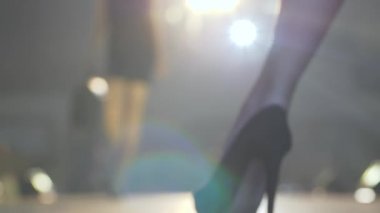 Elinde torbayla rahat ayakkabılar giyen profesyonel model lambaların aydınlatılmasıyla podyuma çıkıyor.