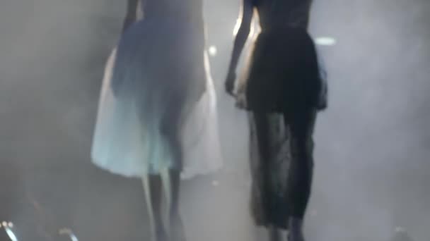 Smala silhuetter av modeller går längs catwalk under en modevisning på bakgrund av ljus och rök — Stockvideo