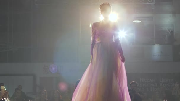 Конкурс красоты, шикарная женщина с короной на голове и длинным платьем идет вдоль сцены освещается прожекторами — стоковое видео