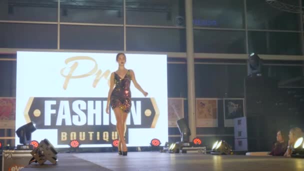 Šaty show, štíhlá mladá žena v lesklé koktejlové šaty na pódiu s jasným reflektorem v týdnu módy — Stock video