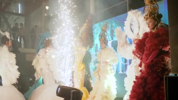 Entretenimento noturno, meninas em traje de carnaval brasileiro brilhante com asas estão no palco perto de fogos de artifício e holofotes — Vídeo de Stock