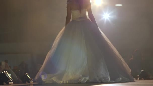 Robes de mariée sur le défilé de mode, belle fille en robe blanche chic marche le long de la passerelle dans les projecteurs éclairage — Video