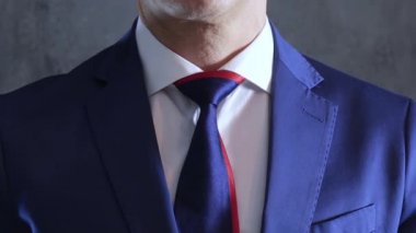 arms of person in blue suit straightens necktie on neck on background of gray concrete wall