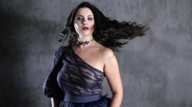 beautiful female with curls and decoration on throat turns on background of concrete wall