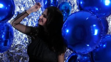 birthday, girl with festive make-up among colored inflatable balloons on background of shiny wall at party