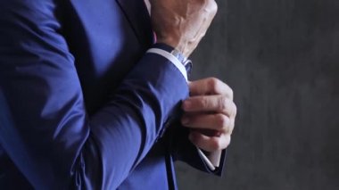 Erkek stili, nişanlısı düğme ve kol düğmelerini arka plandaki gri beton duvardaki gömlek kollarına takıyor.