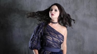 Güzel saç stili ve boynu süslenmiş bir kadın gri duvarın arkasında dönüyor.