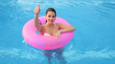 Havuz kenarında durmakta olan pembe şişme yüzüklü bir kadının pozitif hareketi