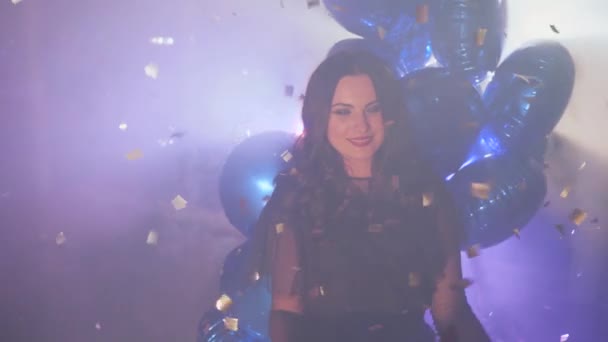 Festive mood, emotional girl holding gift box with bow among shiny sparkles and mist in backdrop of inflatable balloons — Stockvideo