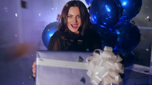 Gift box with bow in hands of happy female amid sparkling confetti and fog against backdrop of inflatable balloons — Stock Video
