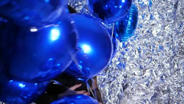 Праздник леди с искренней улыбкой среди надувных воздушных шаров на фоне блестящей стены, украшенной фольгой — стоковое видео