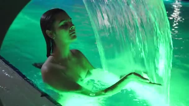 Disfrutar de la hembra en cascada refrescante en la piscina en la noche de verano en el complejo — Vídeos de Stock