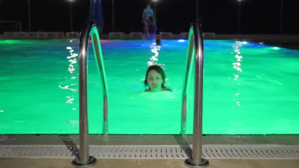 Menina sexual em maiô Sai água segurando a escada junto à piscina à noite — Vídeo de Stock